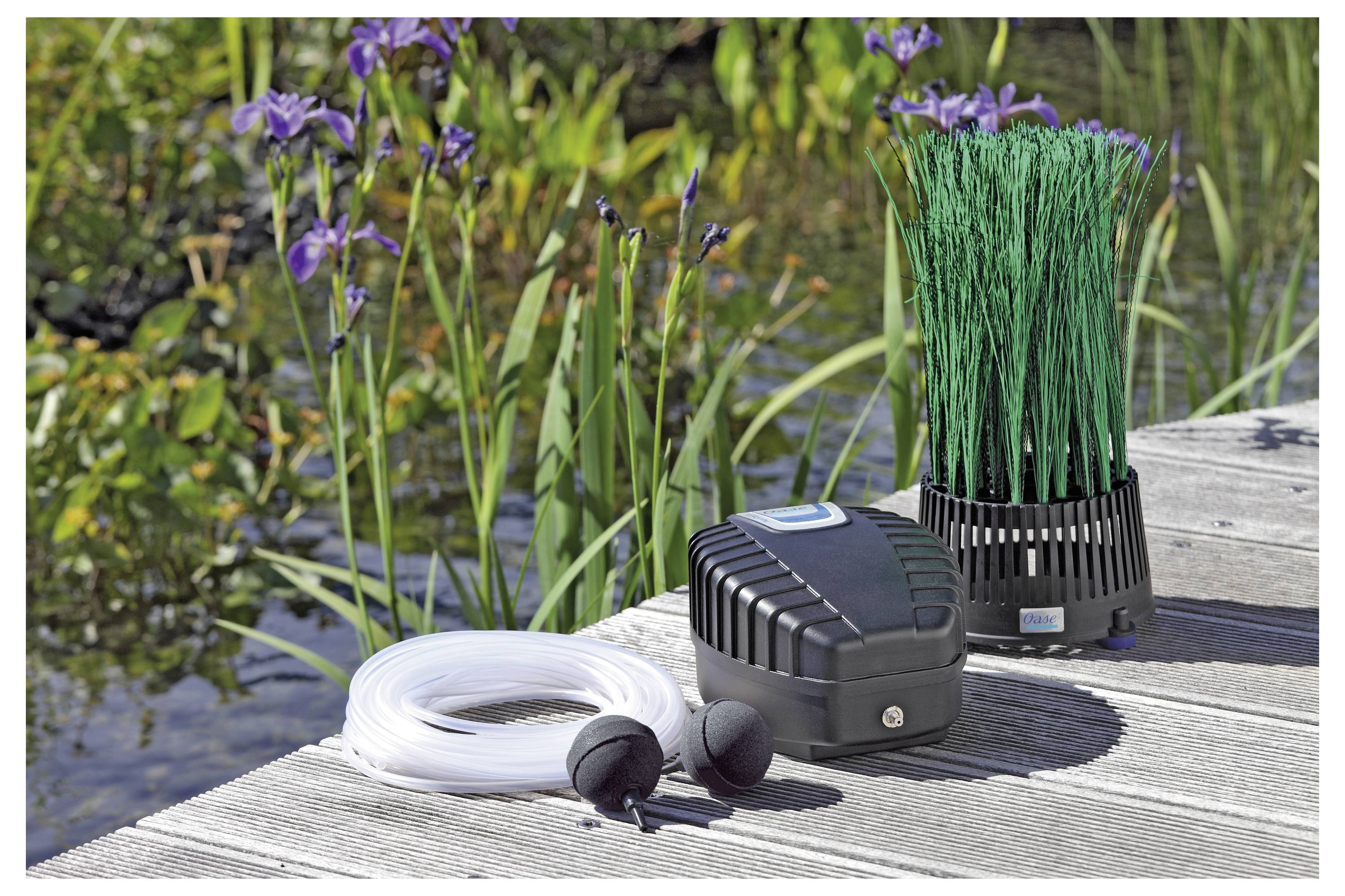 Pond aeration system with pump, tubing, and filtration unit on wooden decking near plants and water, enhancing oxygen levels for aquatic life.
