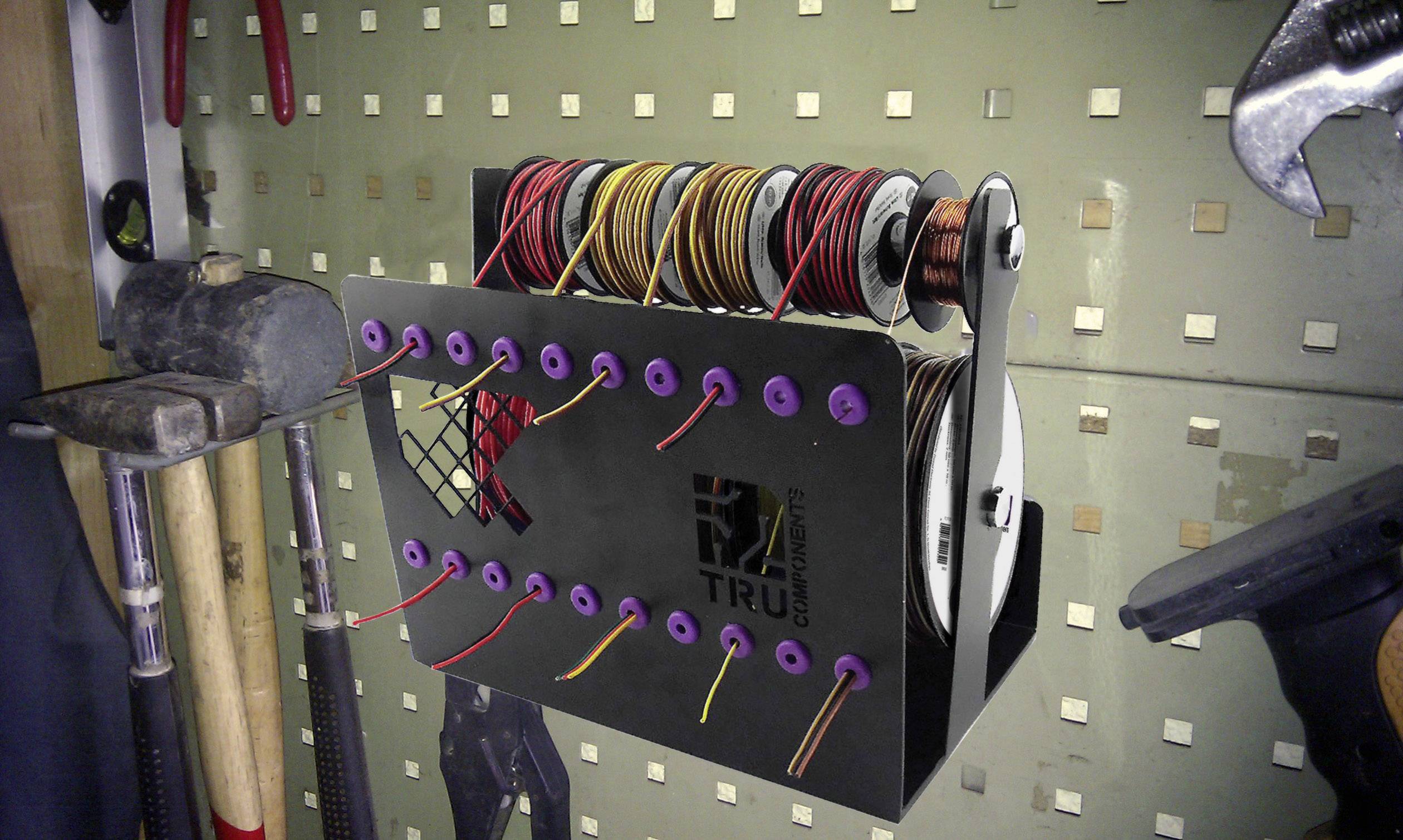 On a tool shelf, framed by hammers and spanners, a cable holder is mounted that winds up colourful cables.