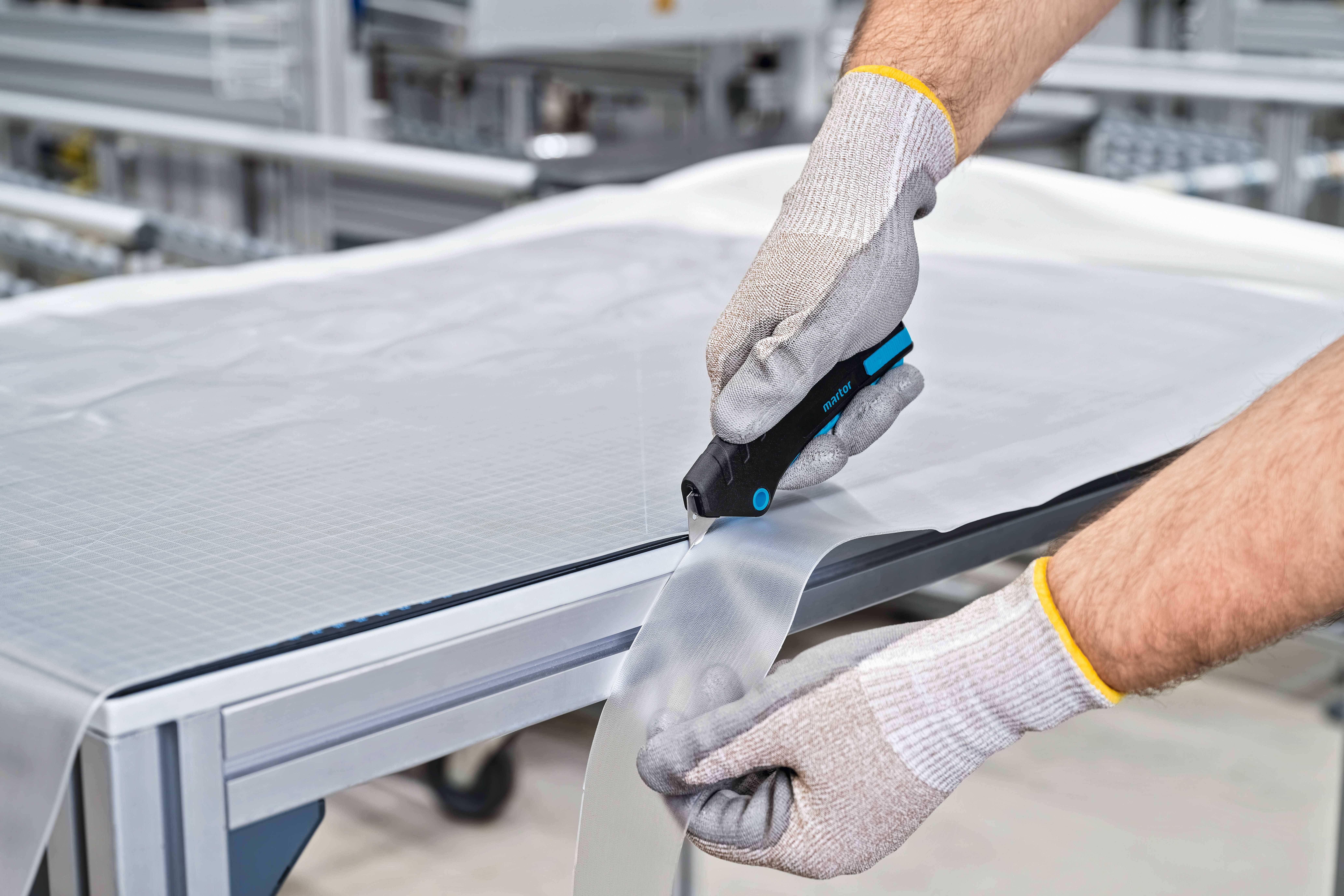 A person wearing protective gloves is cutting solar film on a table with a cutting tool.