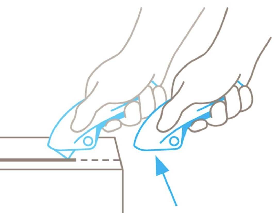 Two hands using safety knives to cut along a dotted line at an edge, with a blue directional arrow marking.