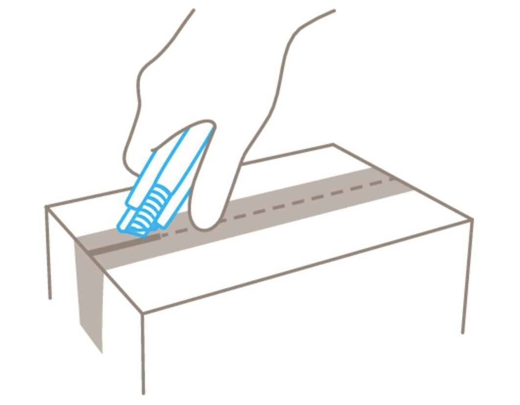 A hand cuts along the dotted line on the top of a cardboard box using a blue utility knife.