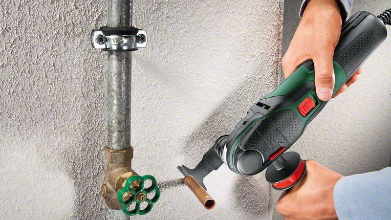 A person is using an electric tool to cut a metal pipe near a tap on a wall.