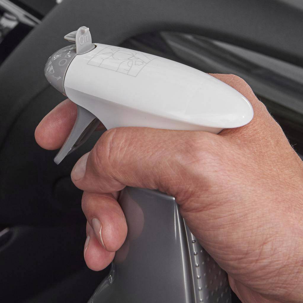 A hand holds the white handle of an iron with an adjustment selector switch, set to '01'. A blurred ironing board is visible in the background.