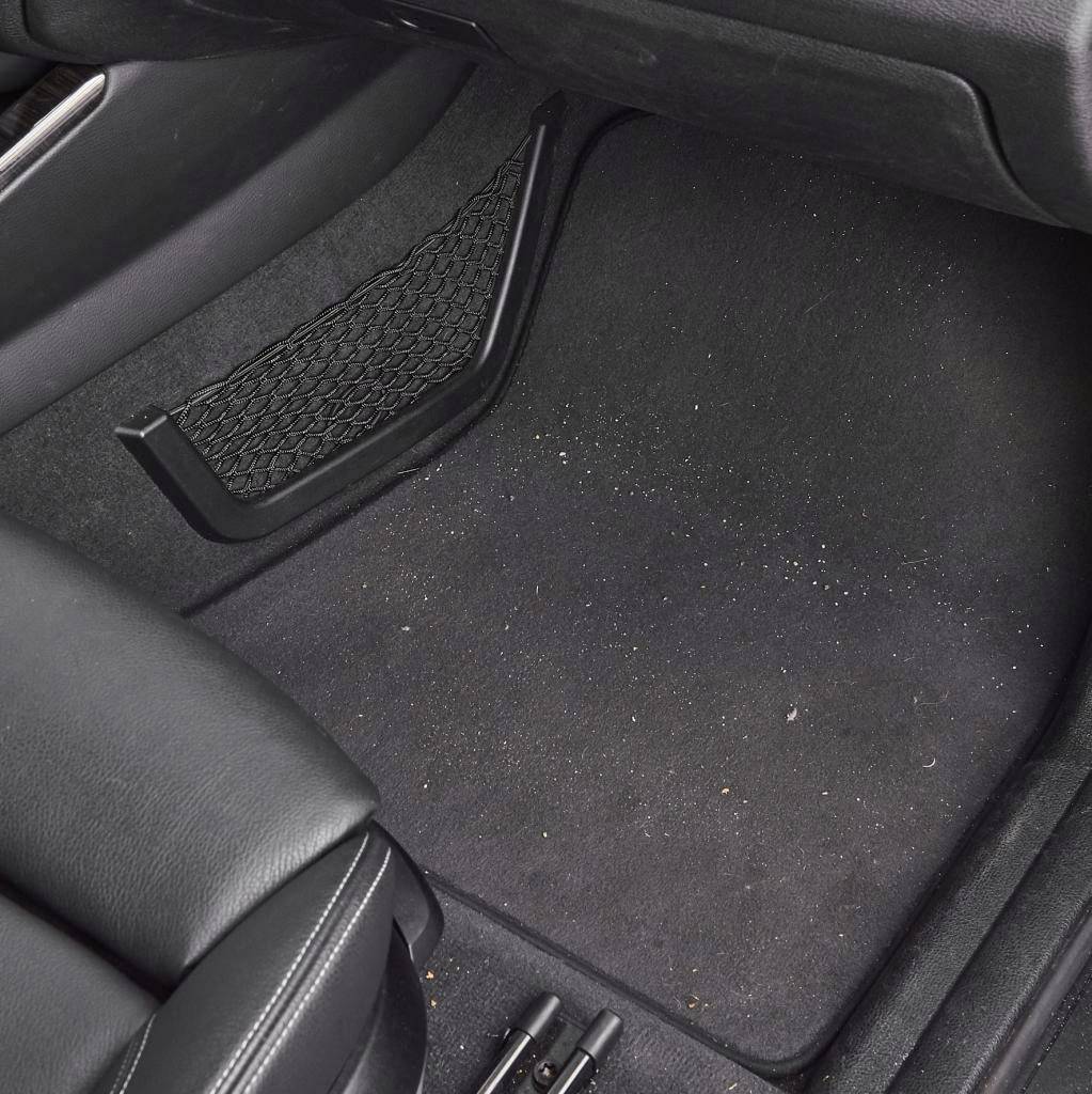 Car footwell with a black floor mat, with a few crumbs and dirt visible.