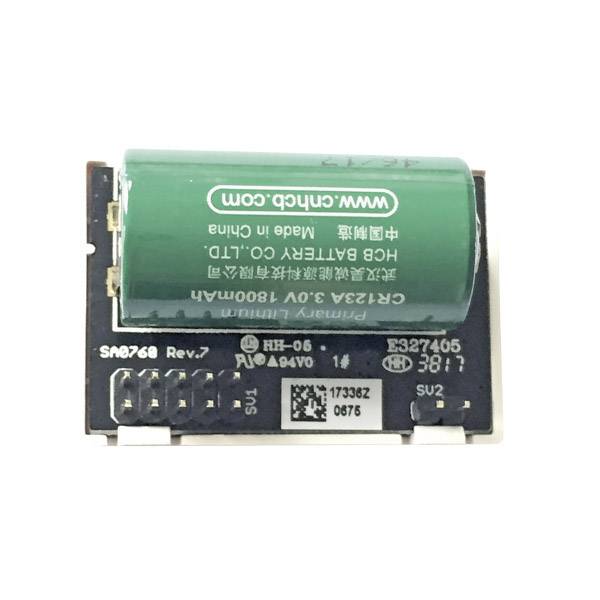 A green battery with the inscription 'Made in China', mounted on a black electronic circuit board with connectors and labels.