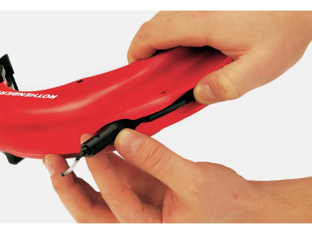 A person holding a red bicycle mudguard, demonstrating how to attach a black cable guide underneath.