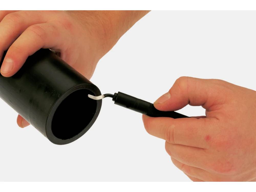 Hands holding a black cylindrical pipe, with one hand using a deburring tool to remove rough edges from the cut end.