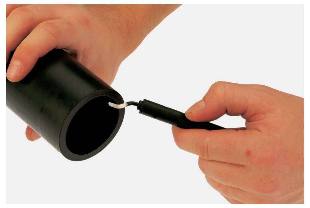 Hands demonstrating deburring a black pipe using a tool; showing the process of smoothing the inner edge of the pipe.