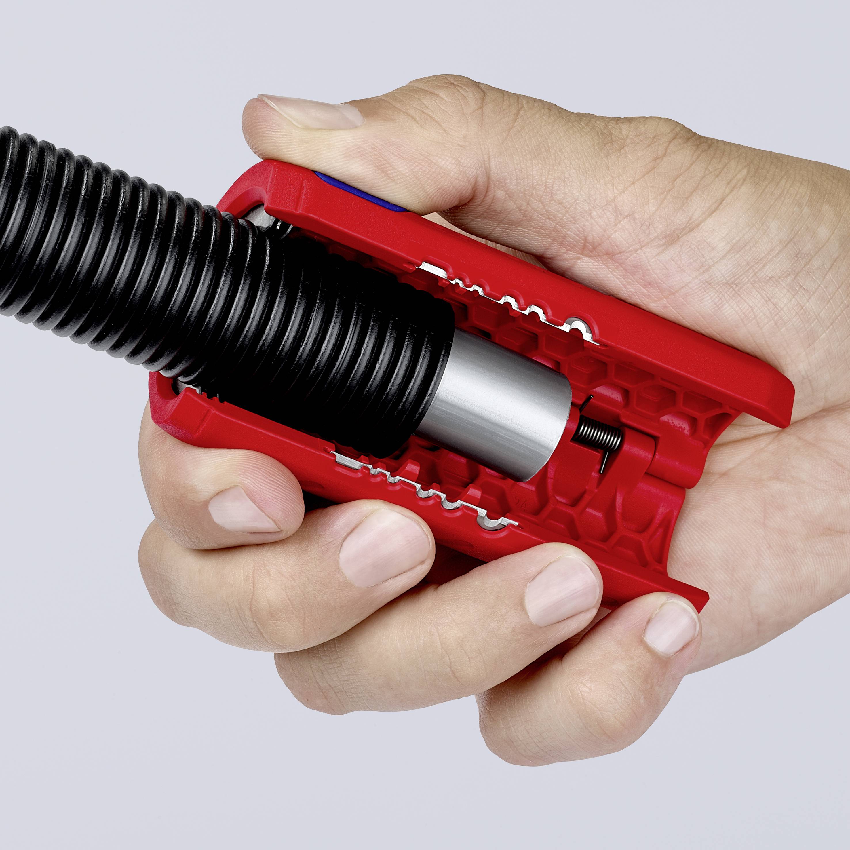 A hand is holding a red cable cutter, cutting through a black cable.