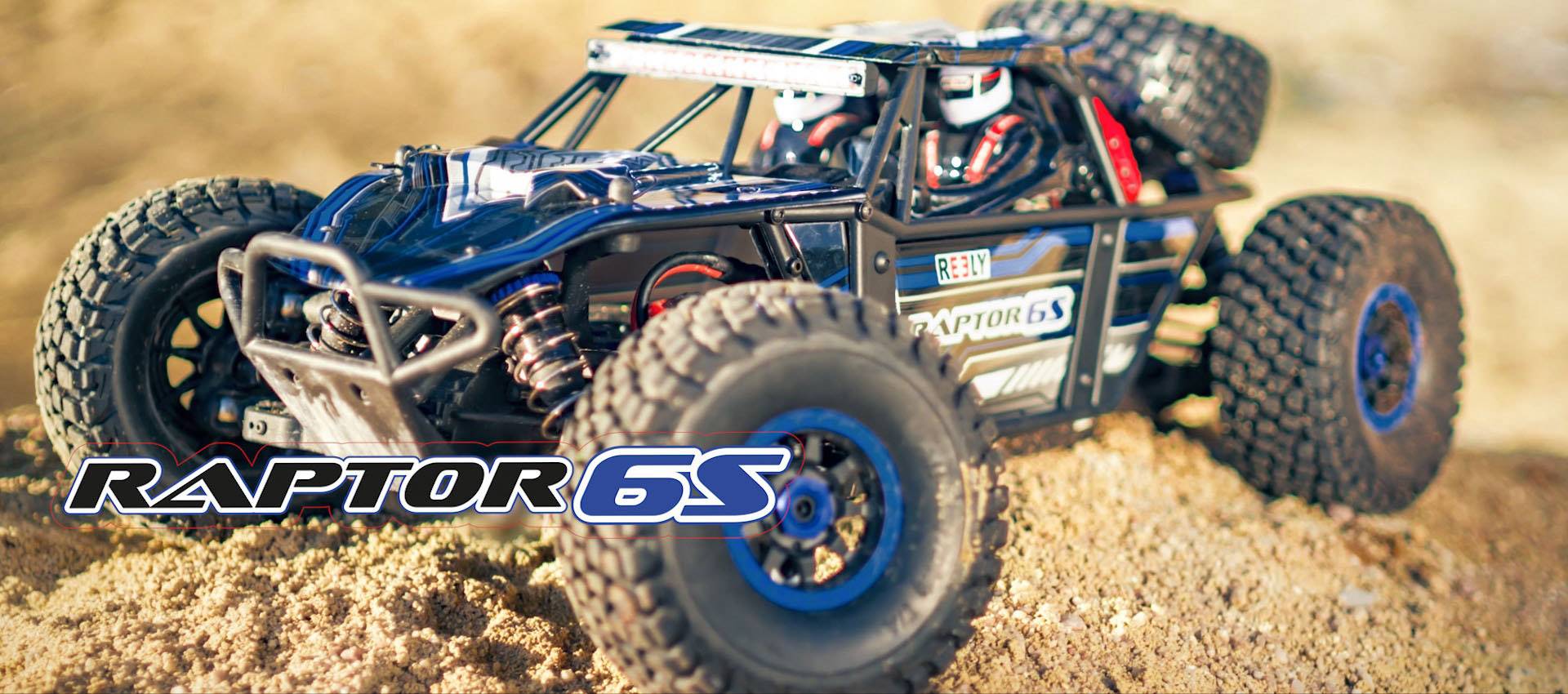 A remote-controlled car with an off-road design drives across sandy terrain. 'Raptor 6S' is written on the bodywork.
