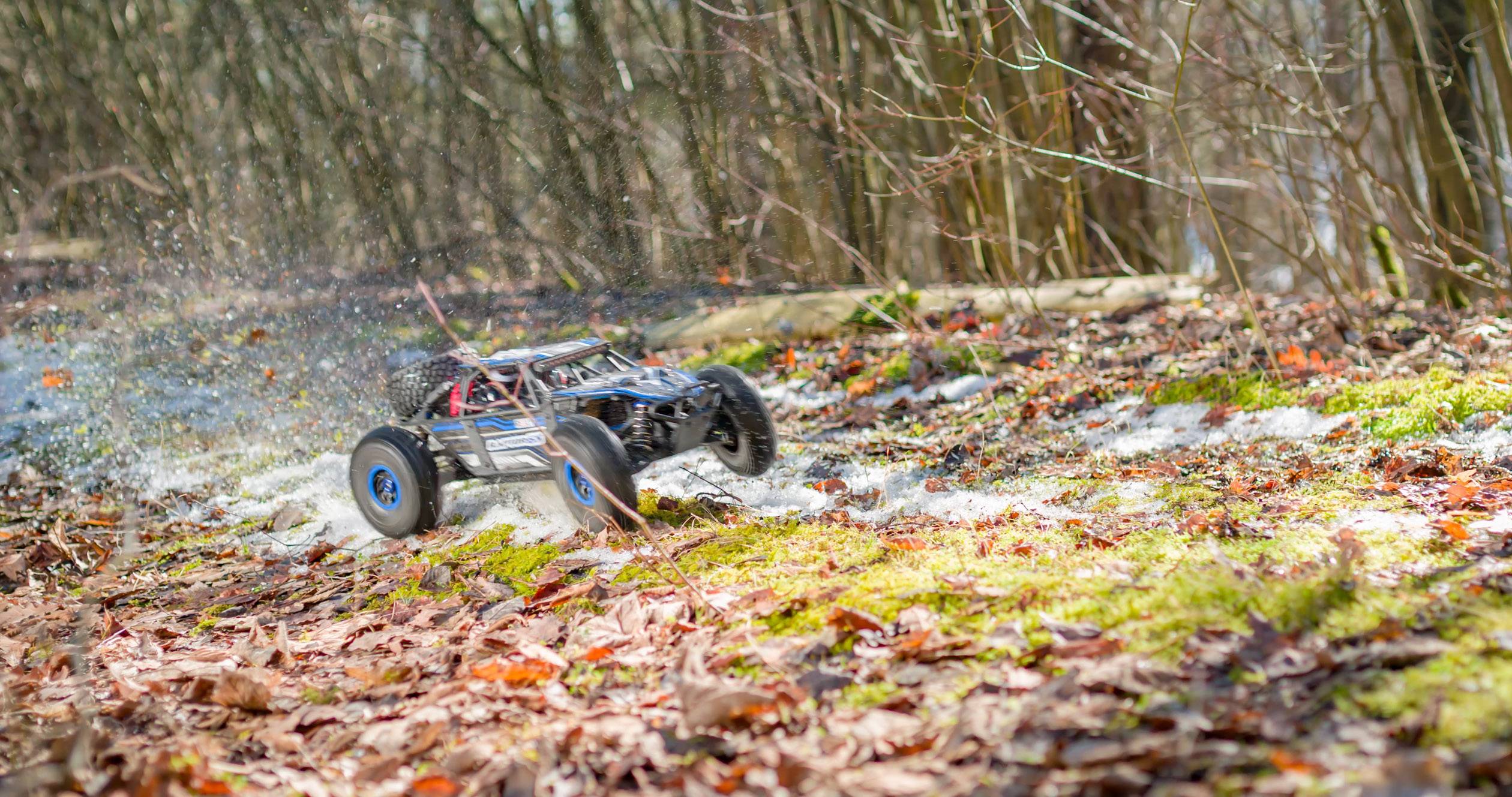 A remote-controlled car speeds through an autumnal forest, whirling up leaves and earth.