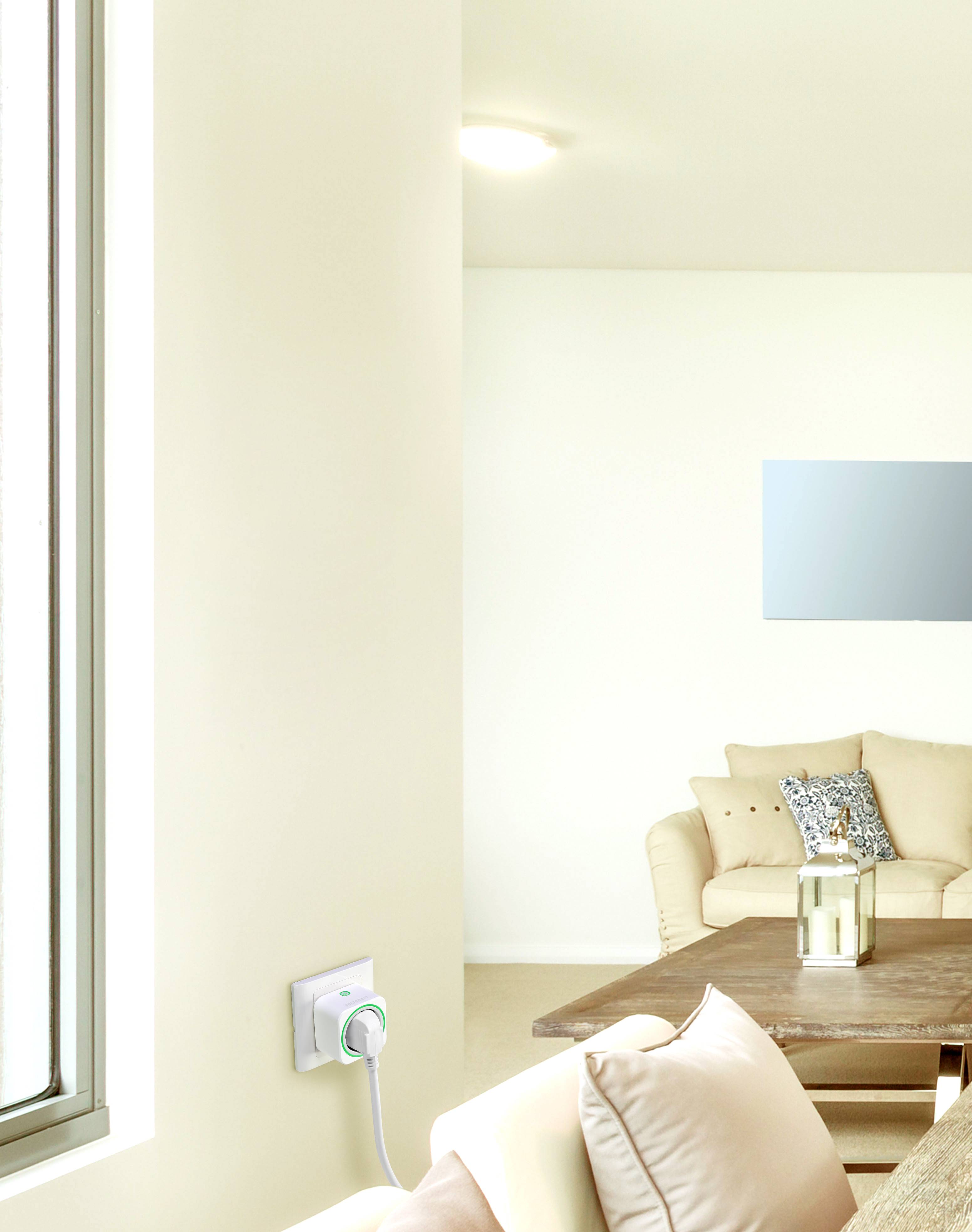 Bright living room with a beige sofa, wooden coffee table and decorative cushions. A modern power strip is mounted on the wall. Large windows allow plenty of light to flood in.