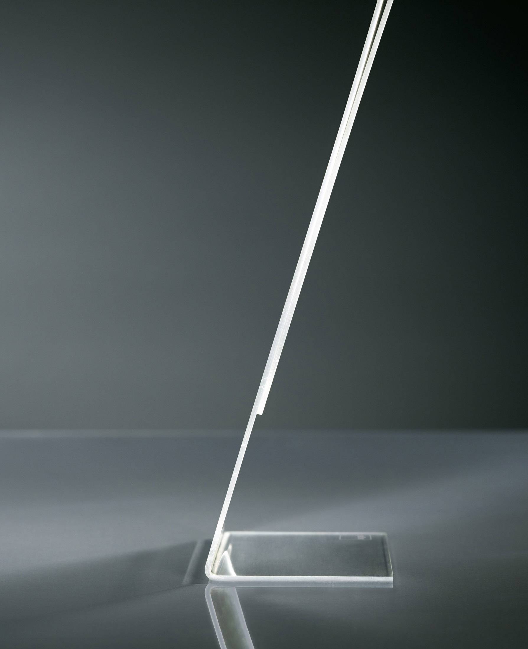 A transparent, narrow, angled object made of glass or plastic stands stably on a flat, rectangular base.