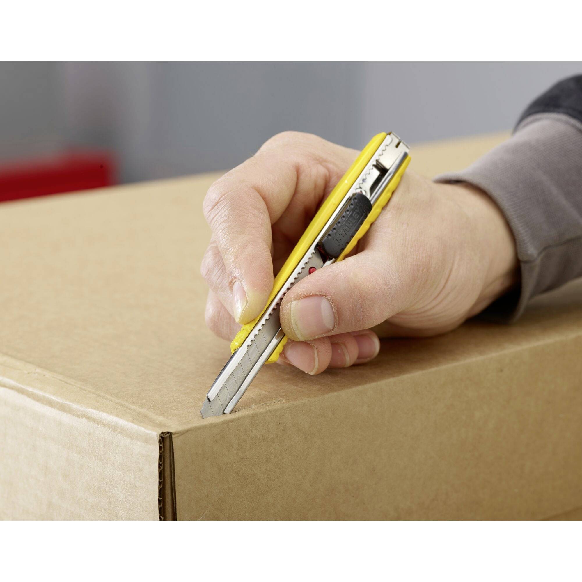 A hand cuts a cardboard box with a yellow Stanley knife.