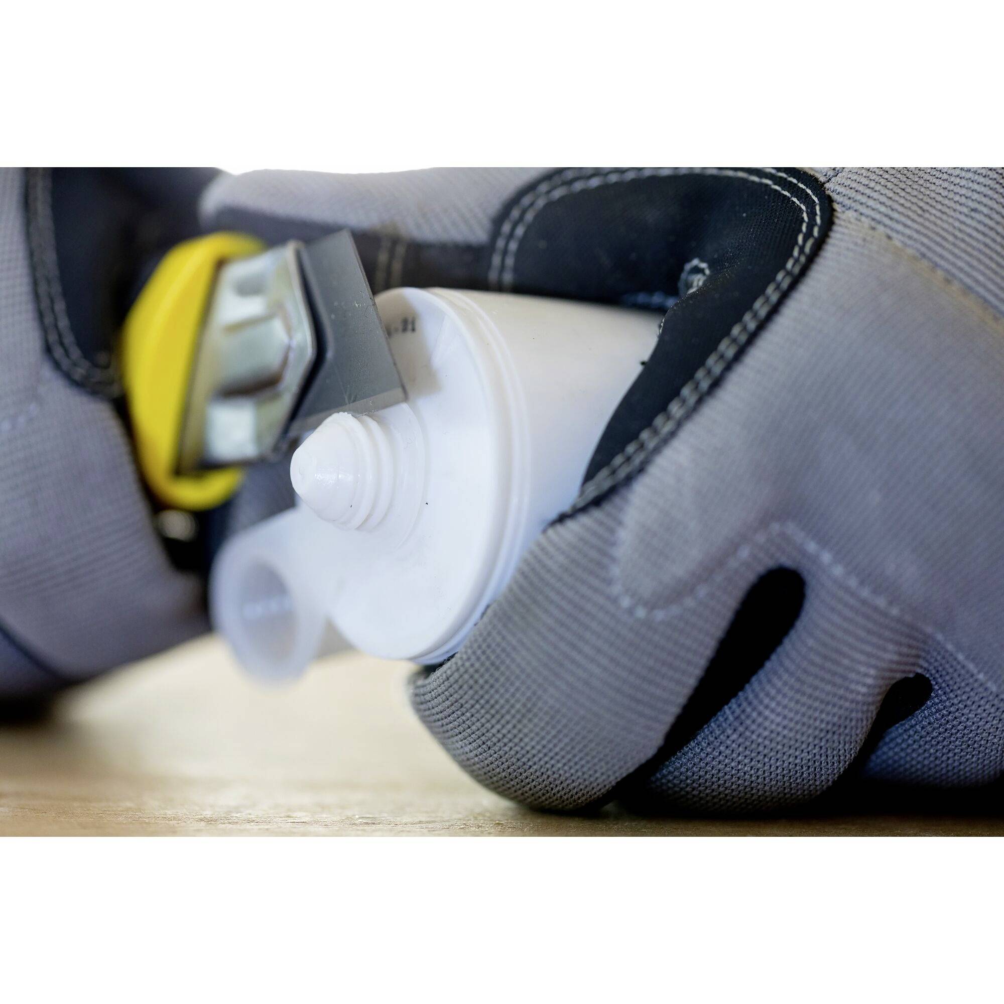 A person wearing grey gloves is holding a tube of glue with a yellow cap.