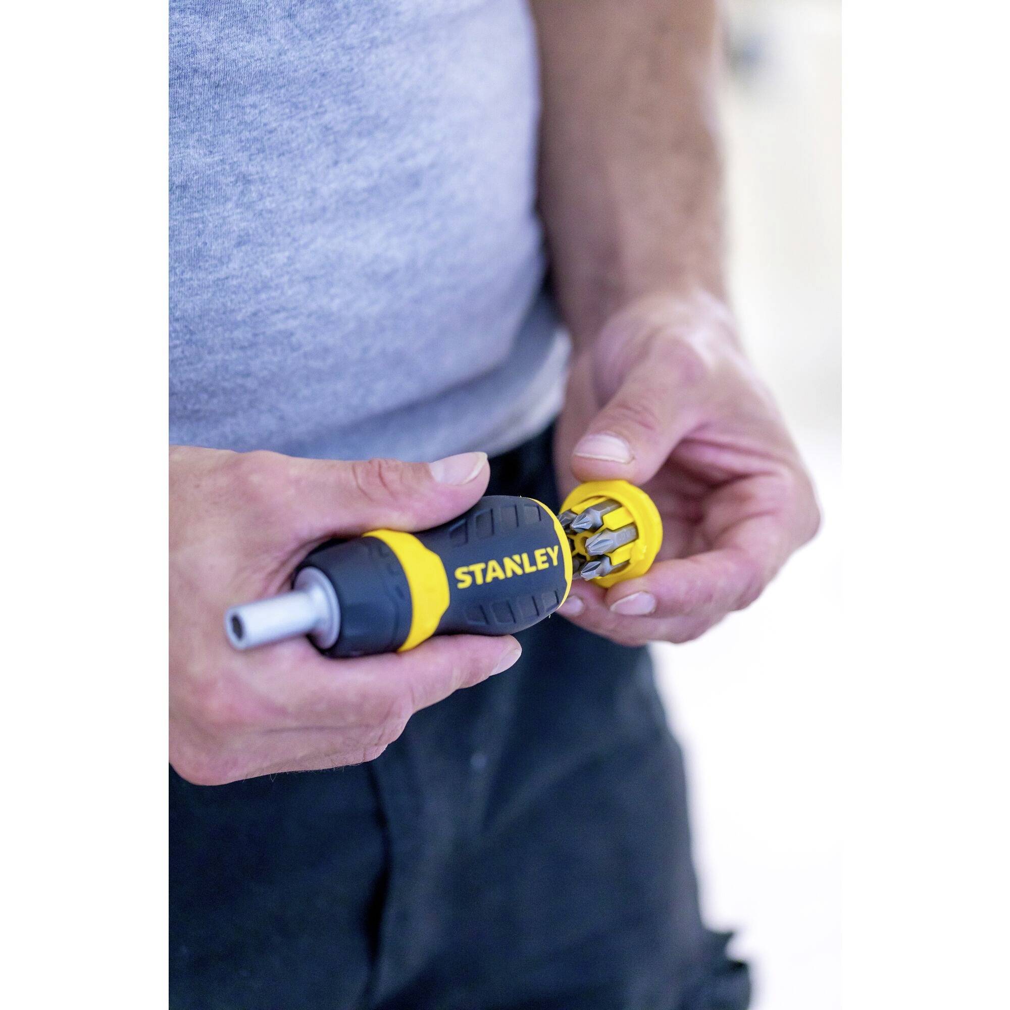 A person is holding a yellow and black Stanley screwdriver and is changing the bit attachments.