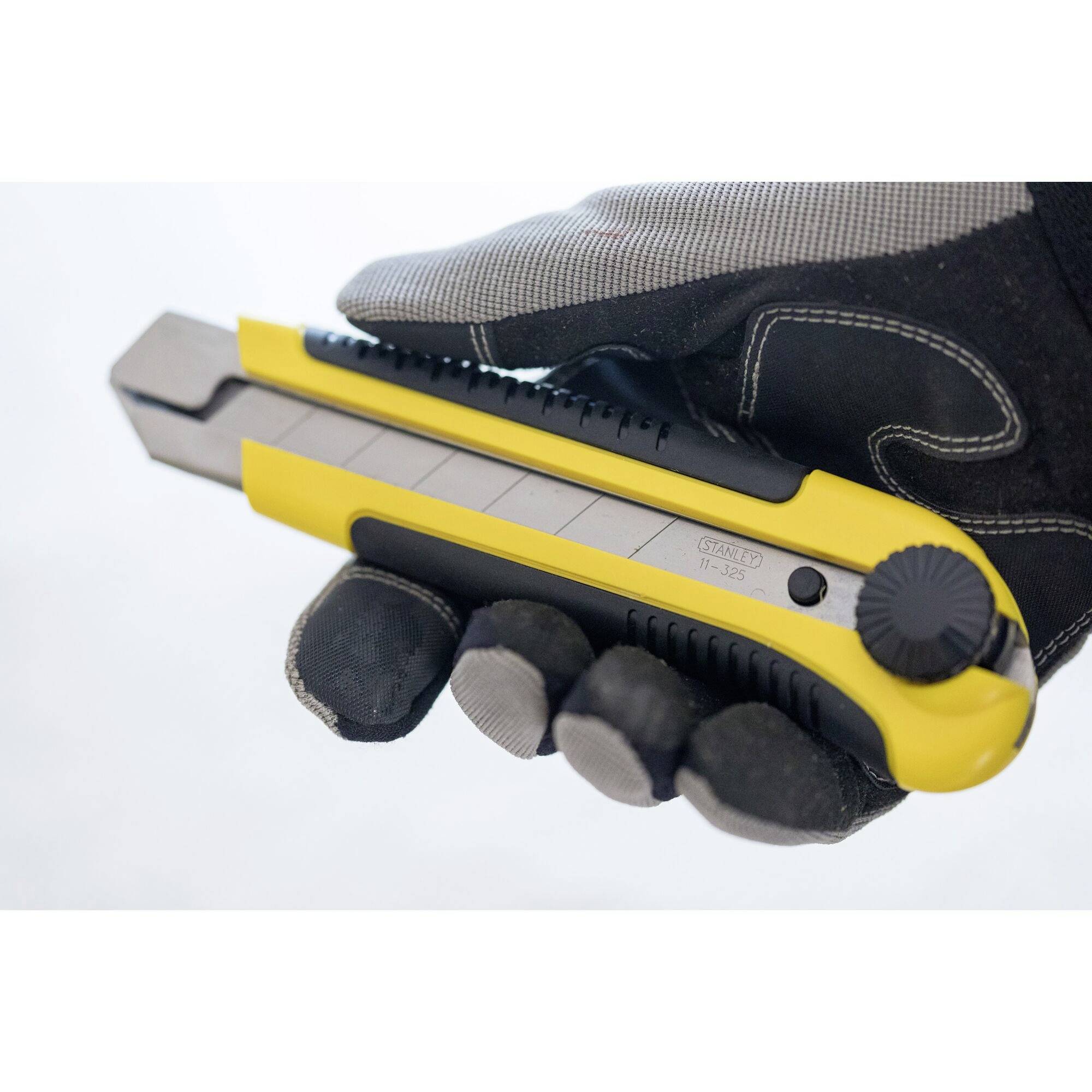 A gloved hand is holding a yellow and grey universal knife with a retractable blade.