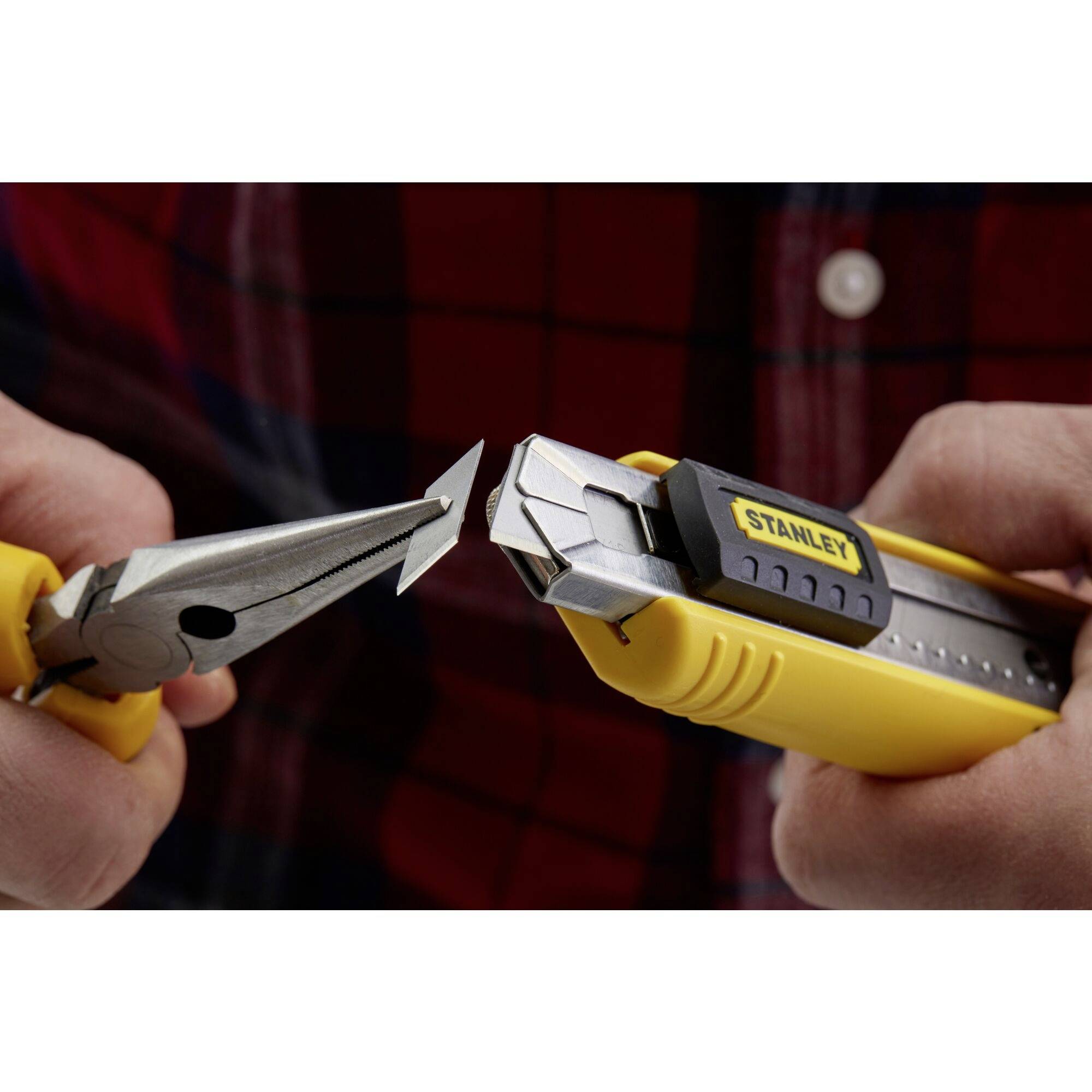 A hand is holding a yellow craft knife with a broken blade, while a pair of pliers grips the blade.