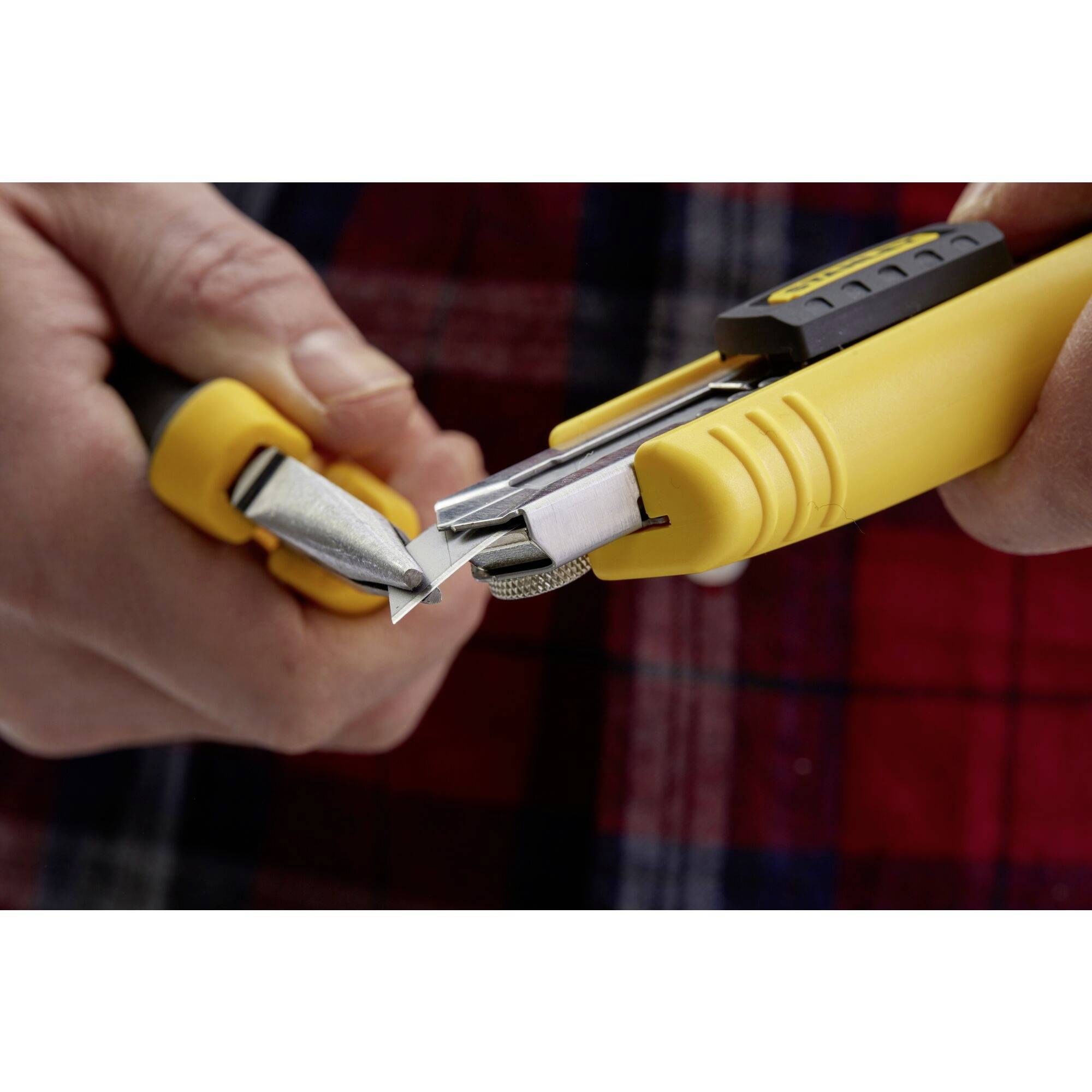 A person is changing the blade of a yellow utility knife. The scene demonstrates safe tool handling methods.