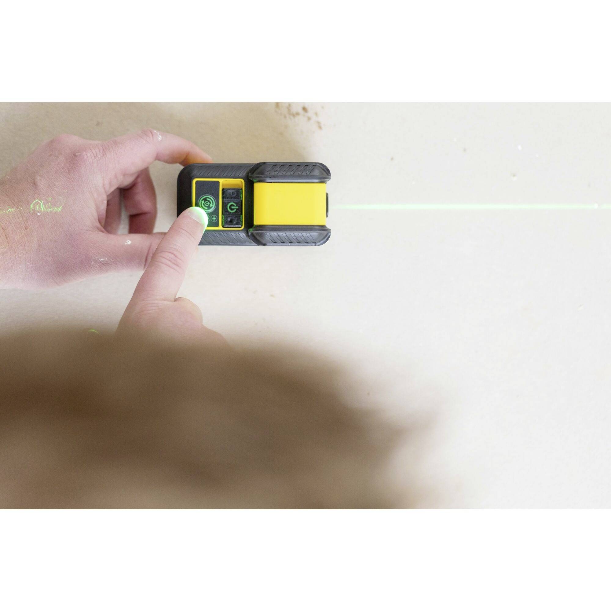 A person is using a wall detector on a light-coloured wall. A green laser beam is indicating a straight line.