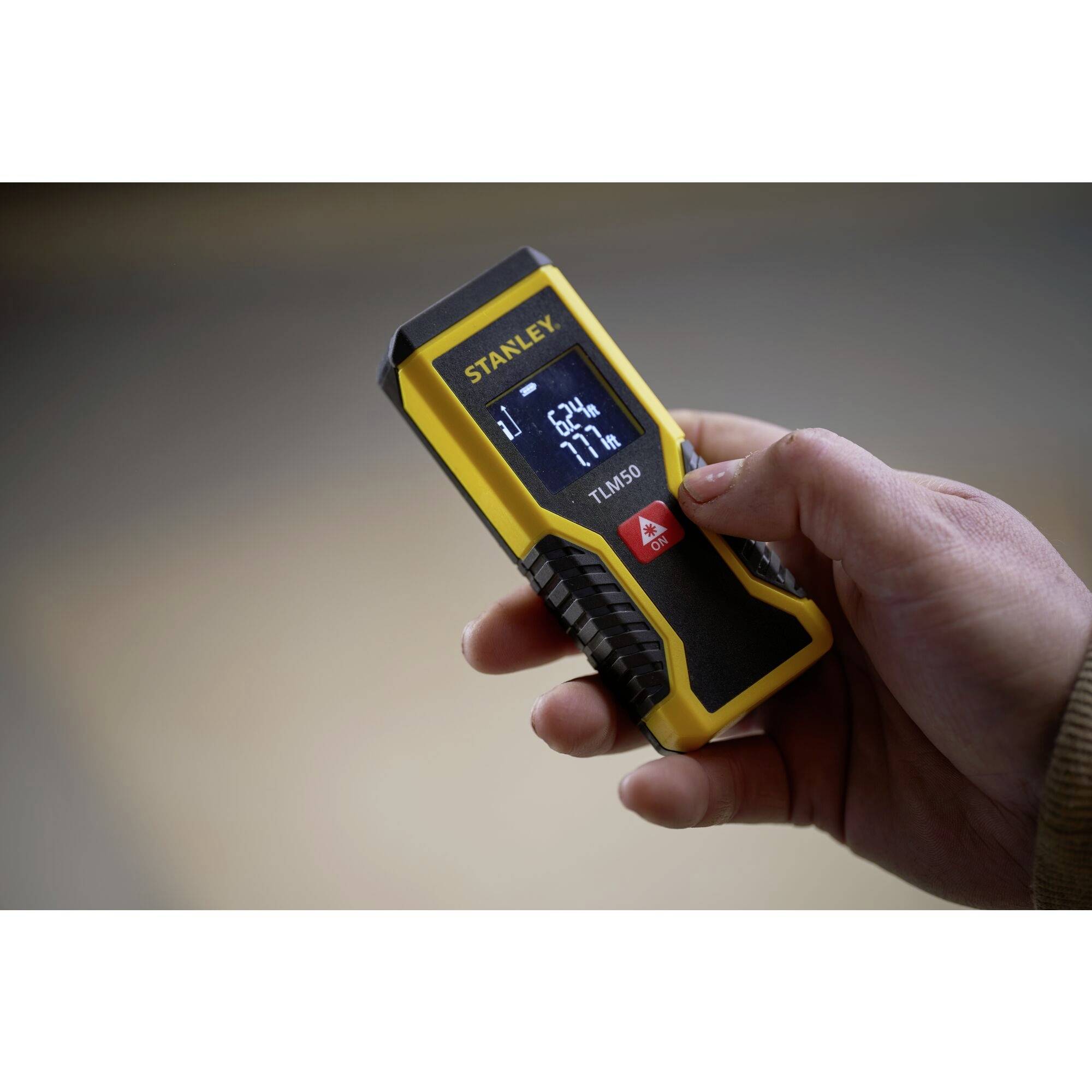 A hand is holding a yellow laser distance measuring device with a blue display showing '21 m', '67%', and other data.