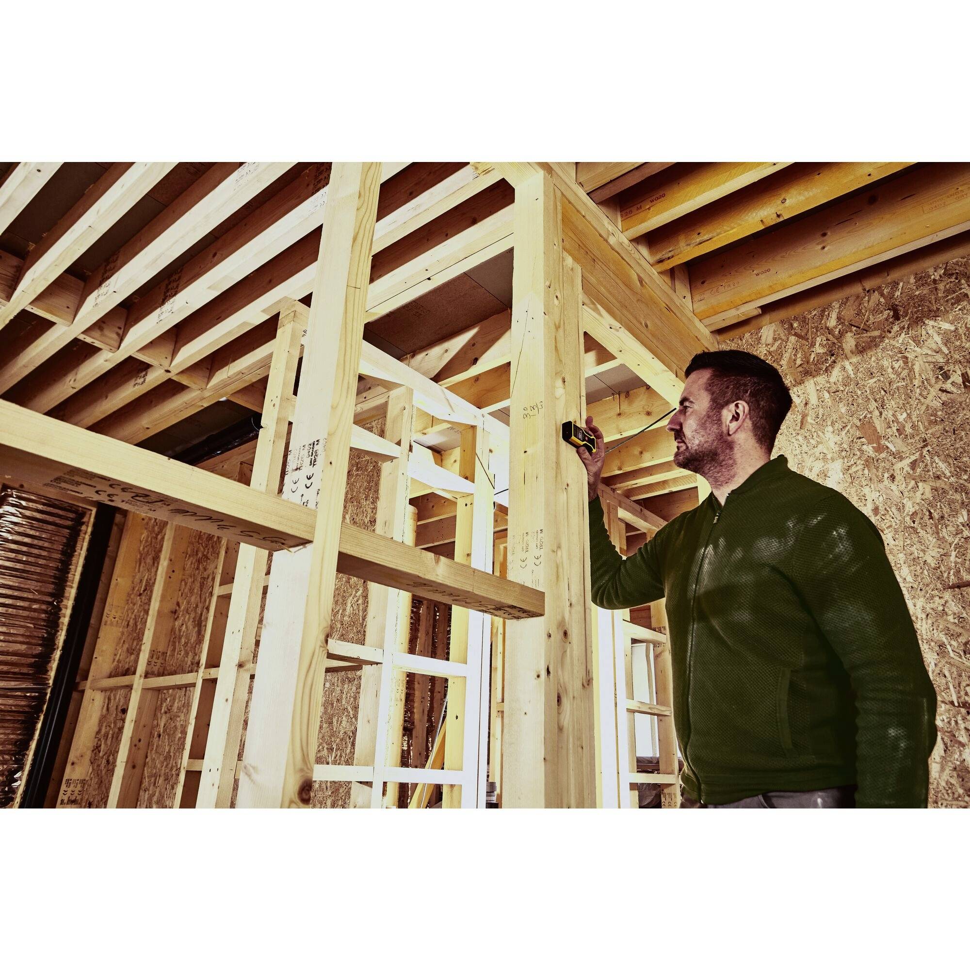 A person is measuring a wooden frame with a tape measure in a room under construction.