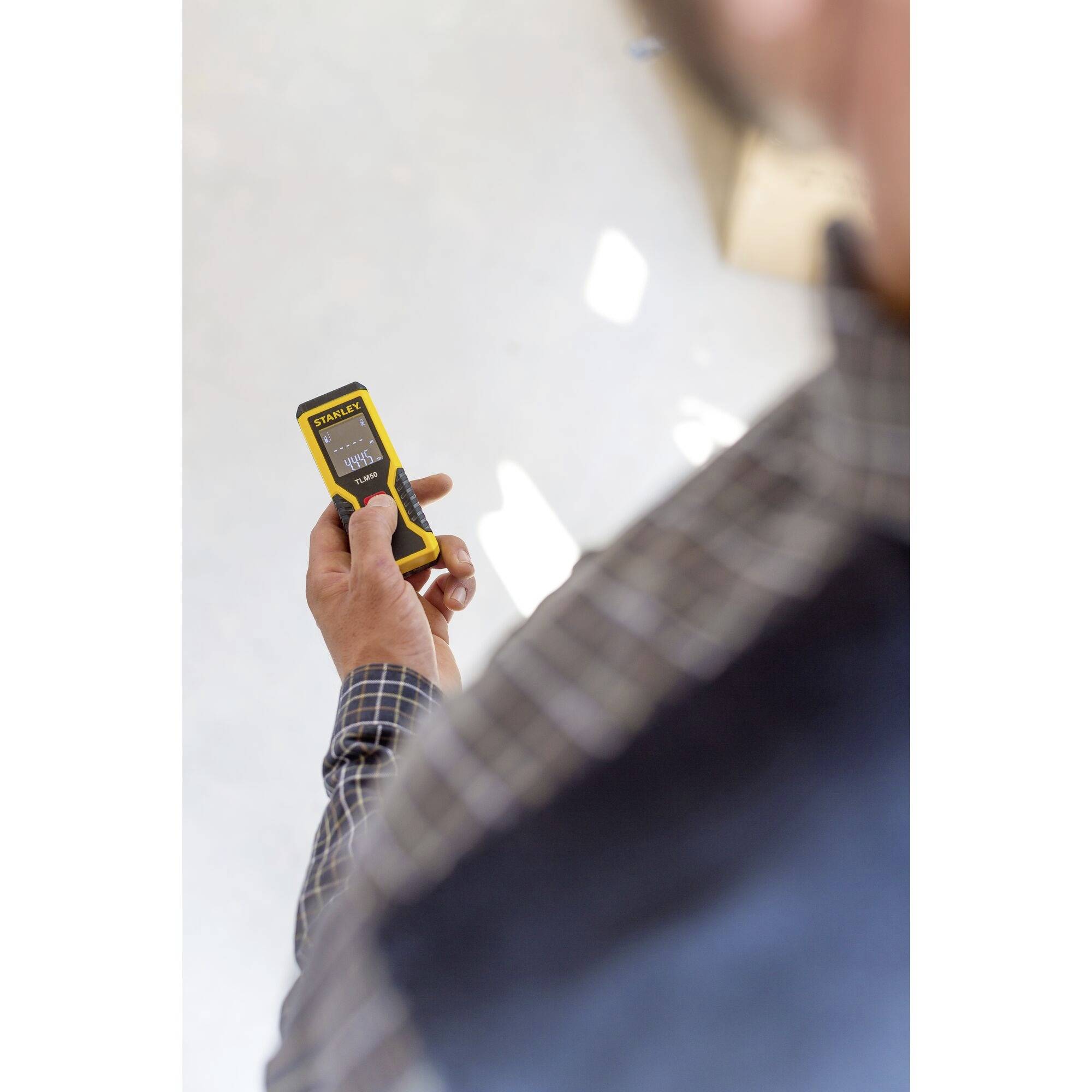 A person is holding a yellow electronic device displaying a distance in metres. The focus is on the hand and the device.
