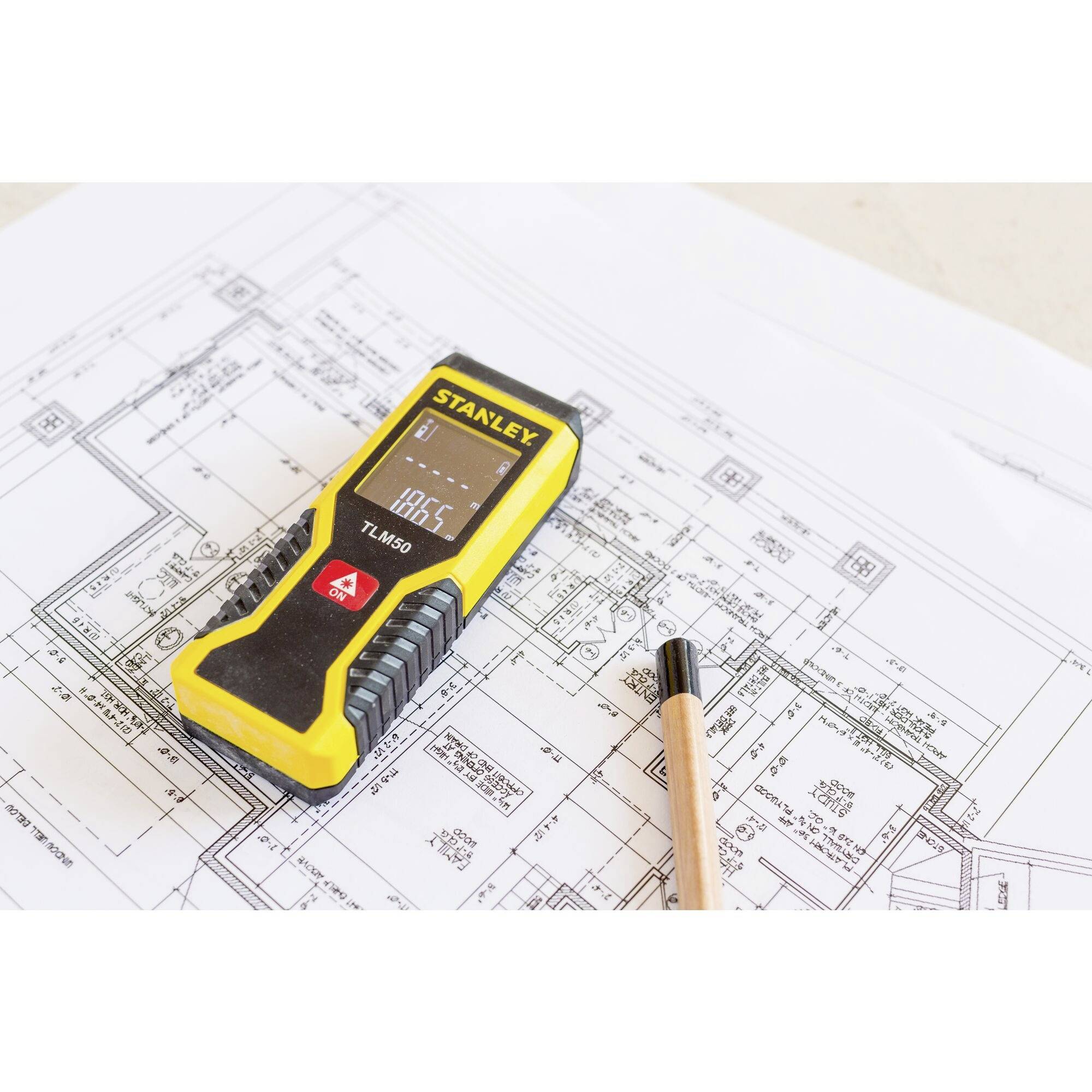 A yellow digital measuring device lies on a blueprint next to a pencil. The device displays '18.65°C' on its screen.