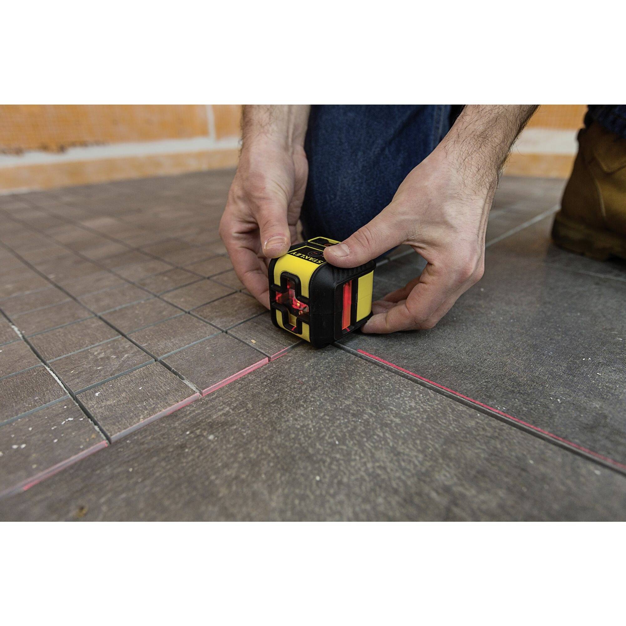 A person is aligning tiles on a floor using a laser tool to ensure precise lines and levels.