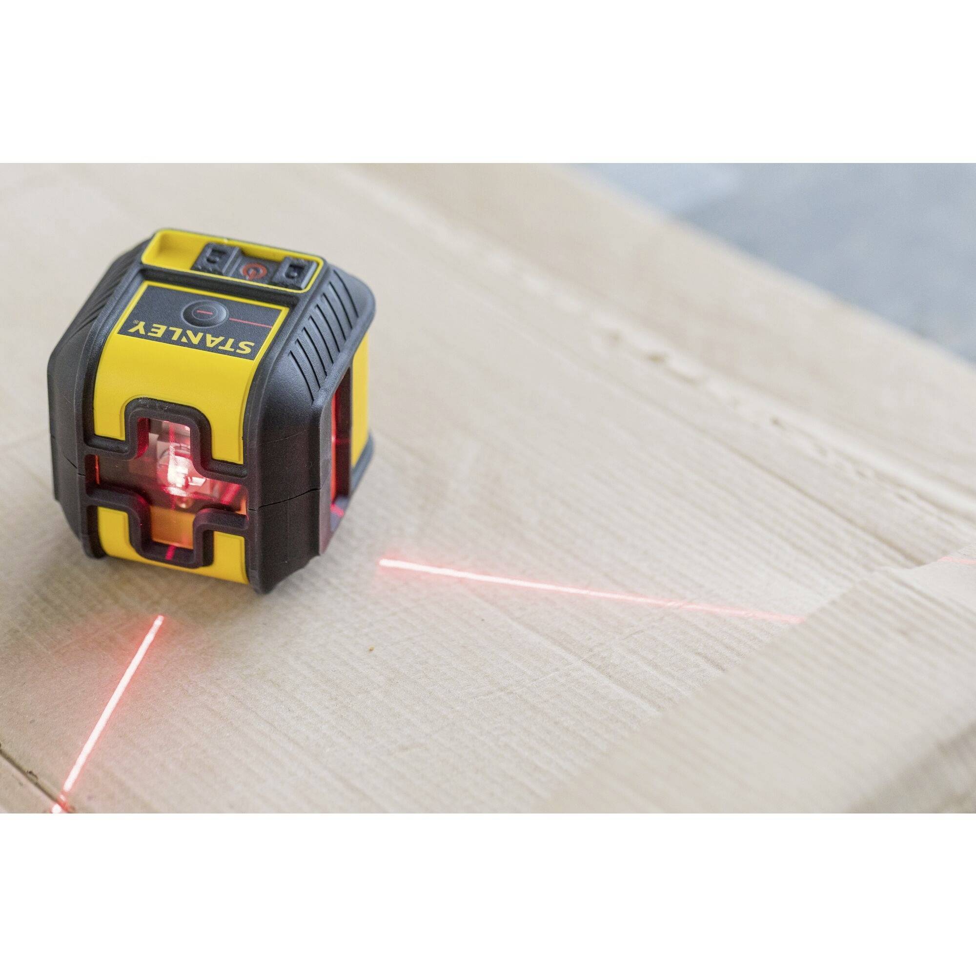 A yellow laser levelling device projects red lines on a wooden floor for precise alignment during construction work.