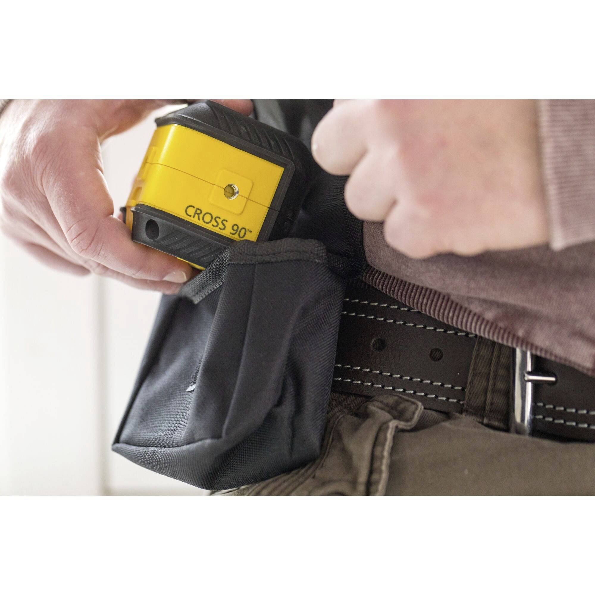 A yellow cross-line laser device is placed into a black tool bag. A person's hands can be seen.
