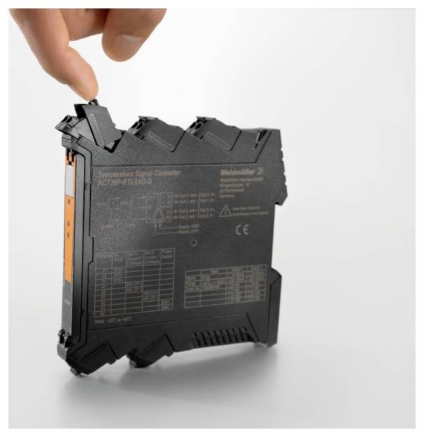 A person's hand is adjusting or holding a compact, black electronics module with detailed labeling, likely used for industrial systems.