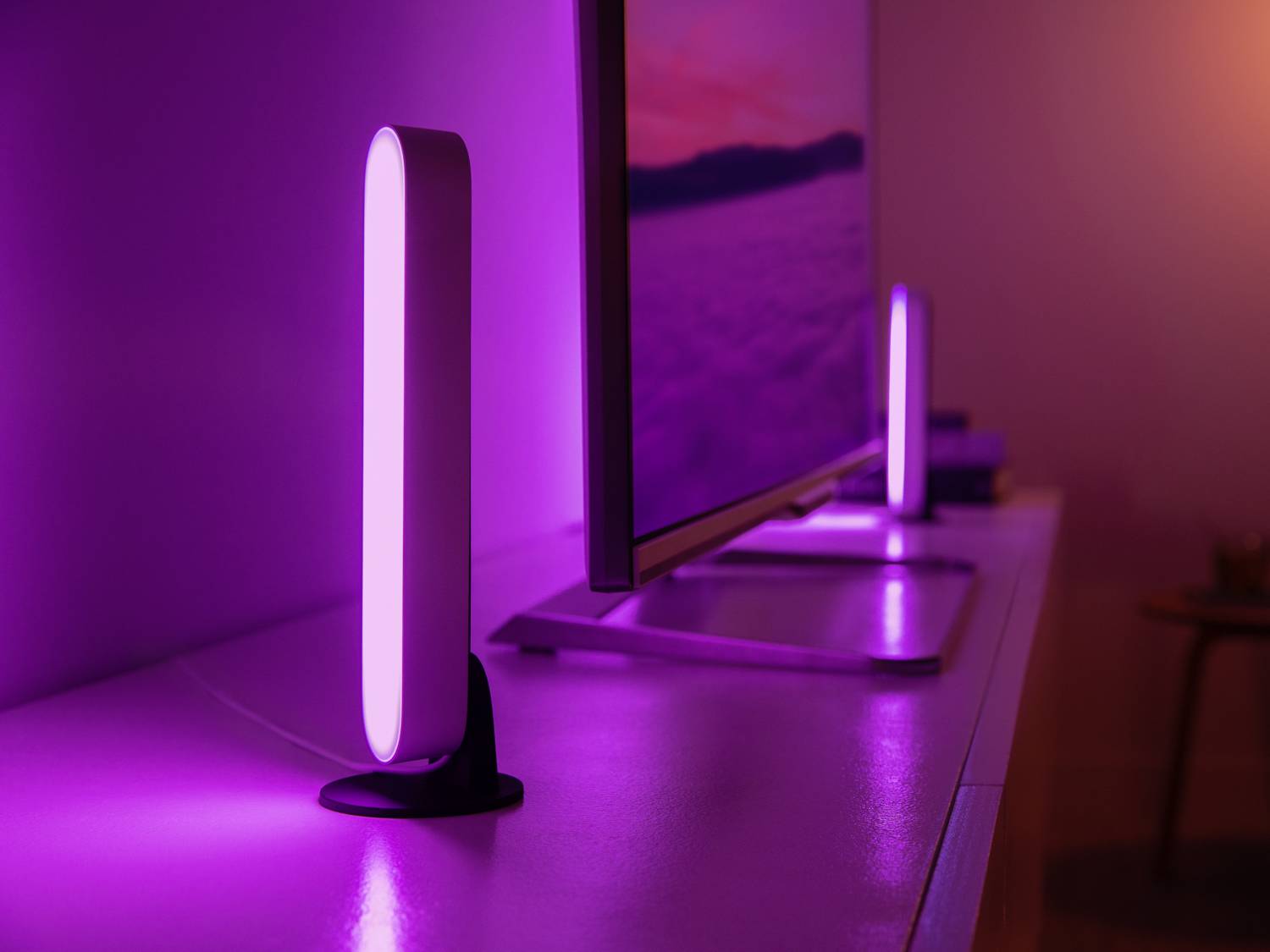 Two purple LED lamps illuminate a room, one on each side of a monitor. The lighting creates a mood-enhancing atmosphere.