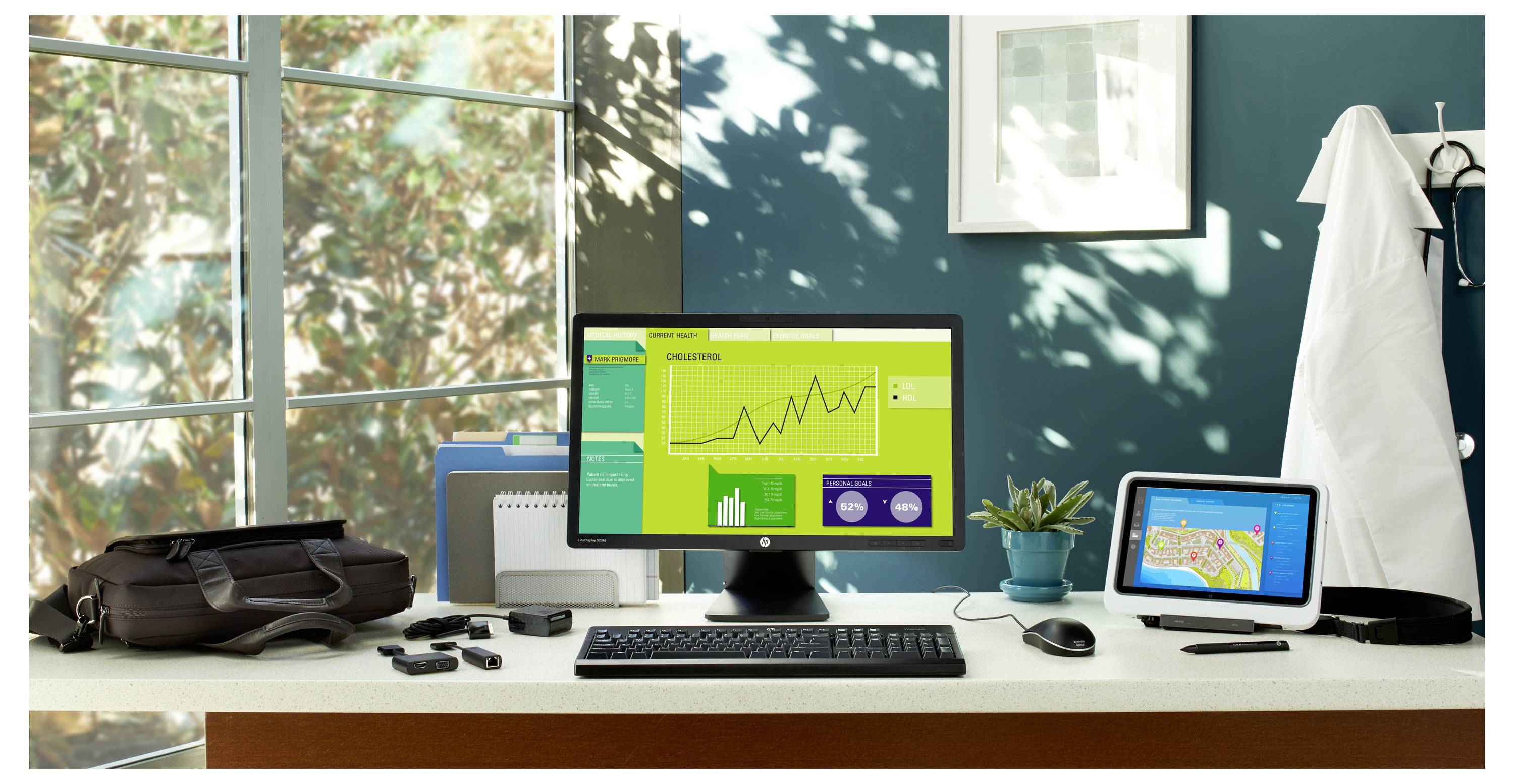 Office desk setup with computer displaying a line graph and statistics, alongside a tablet with a map, surrounded by office items.