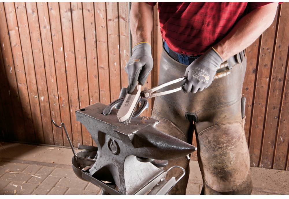 A person is shaping a glowing horseshoe with tongs on an anvil in front of wooden panelling.