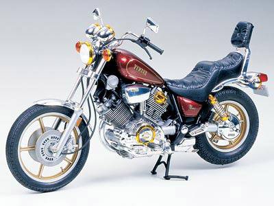 A red motorcycle with chrome details, raised seat, and golden accents stands on a stand against a grey background.