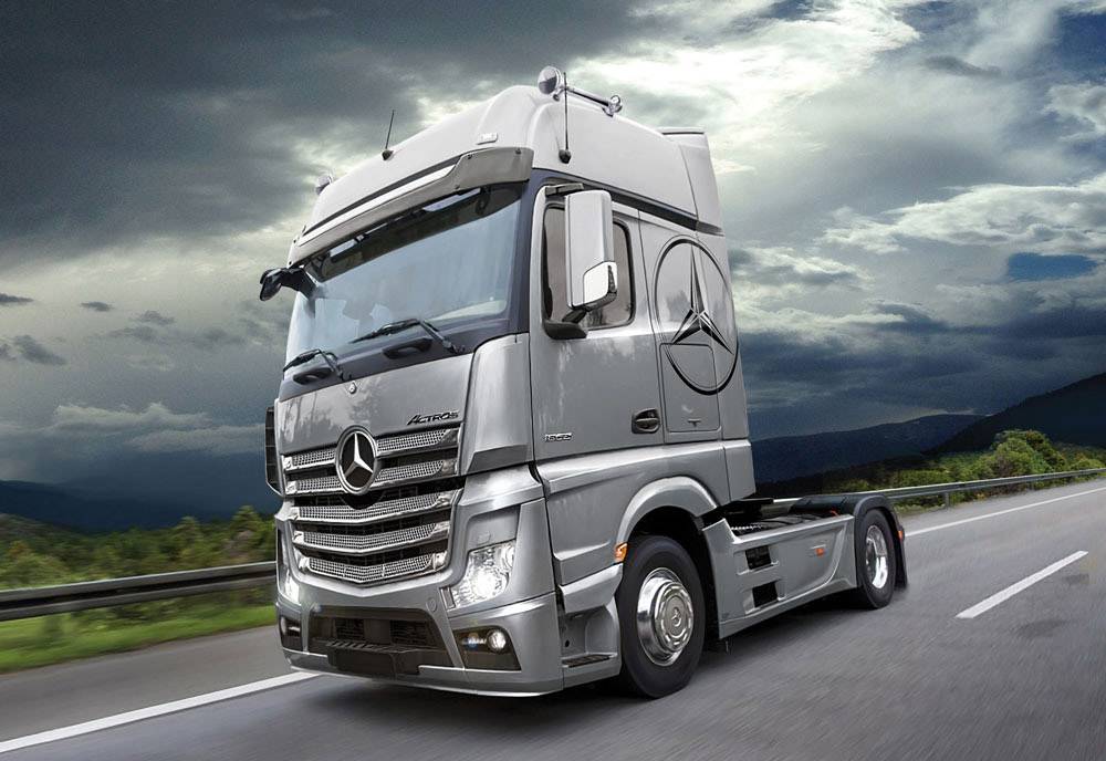 A silver lorry drives alone on an empty motorway with a cloudy sky in the background.
