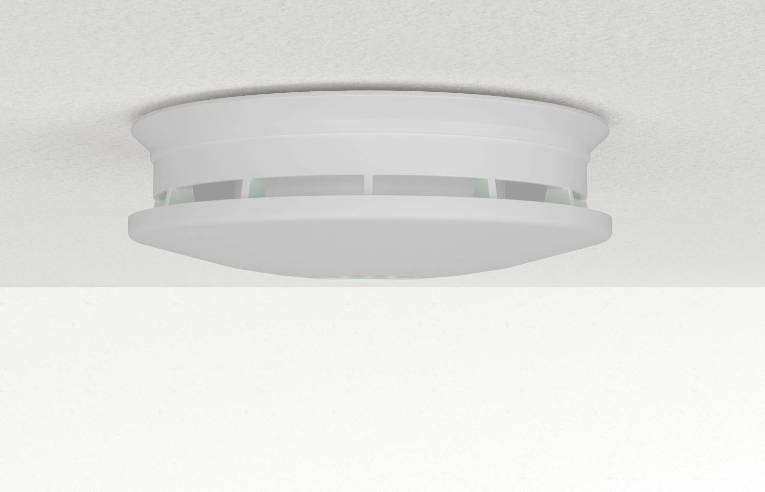 A smoke detector mounted on a ceiling, featuring a round, white design with side vents, typically used to detect smoke and fire.