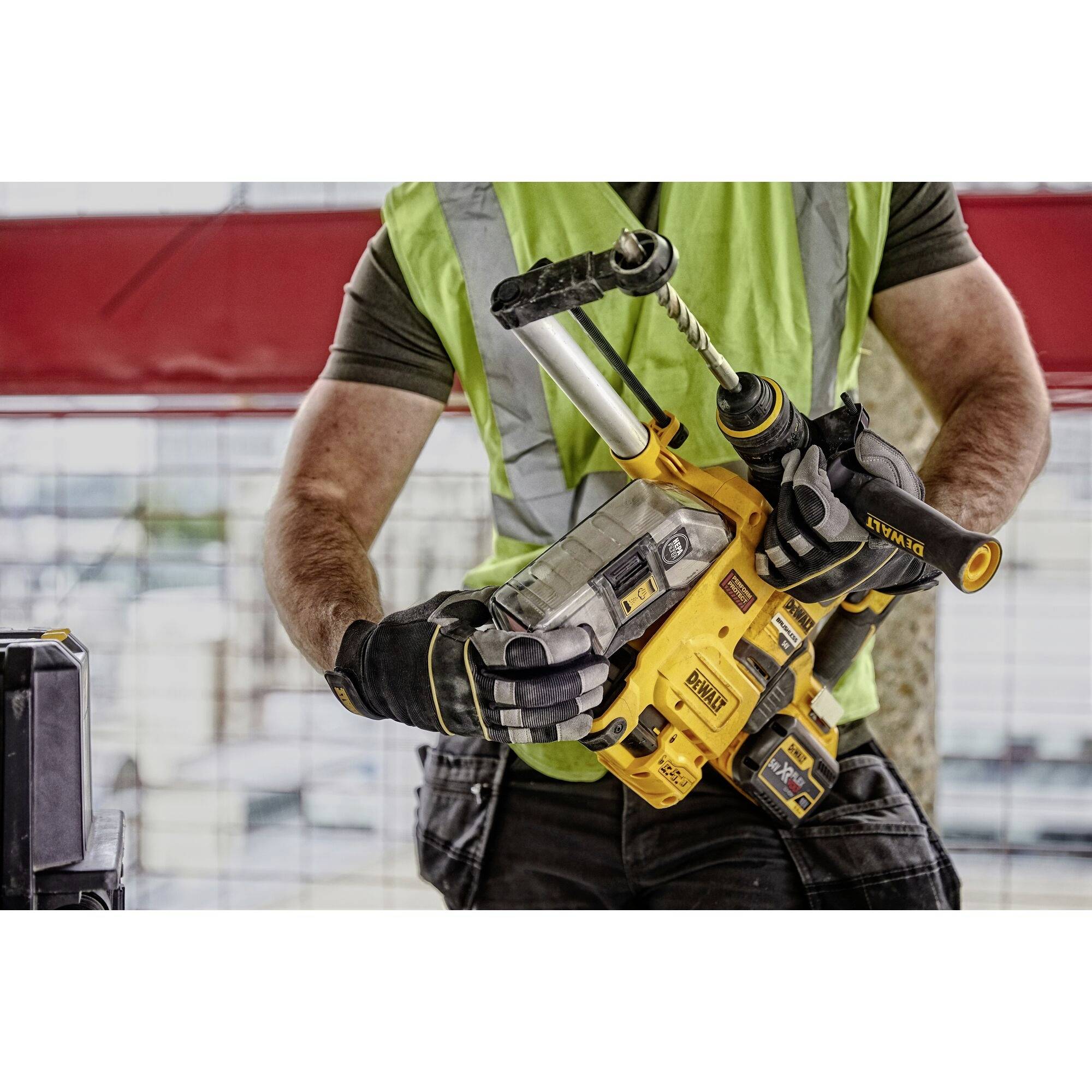 A person in safety clothing is holding a yellow cordless drill on a construction site.