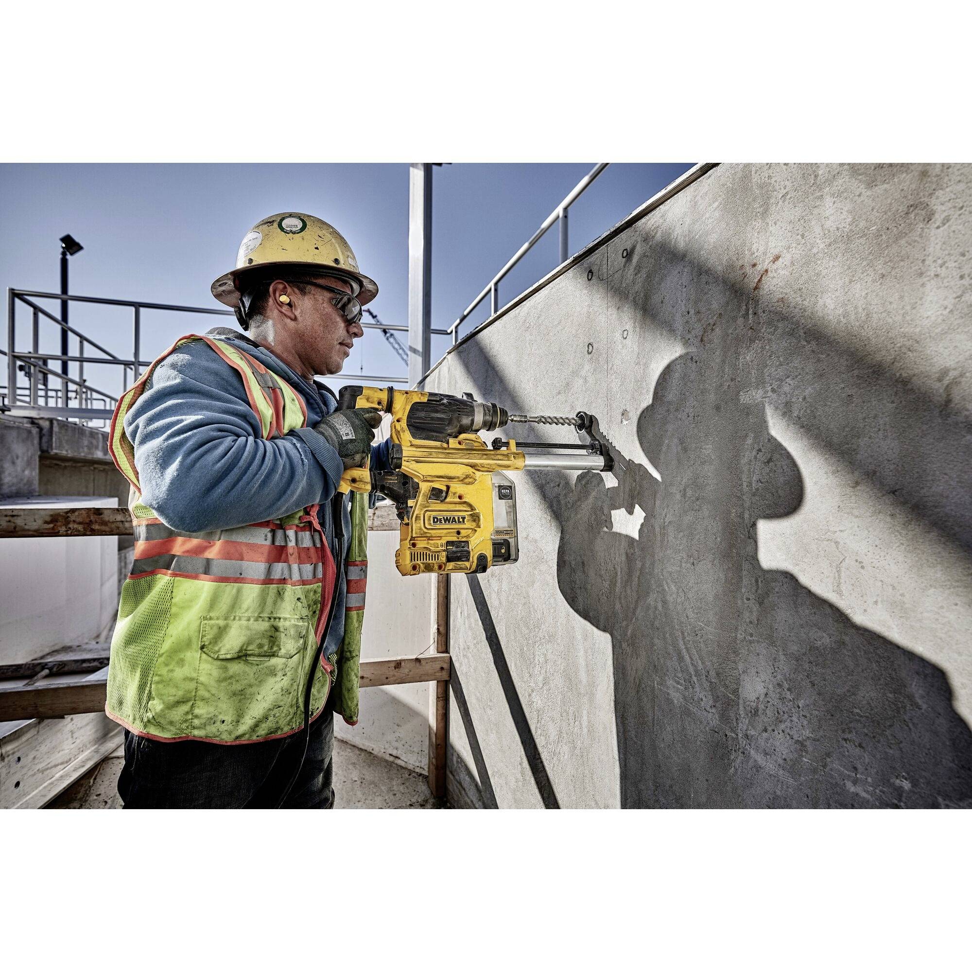 A construction worker is wearing protective clothing and using an electric drill tool to bore holes into a concrete wall.