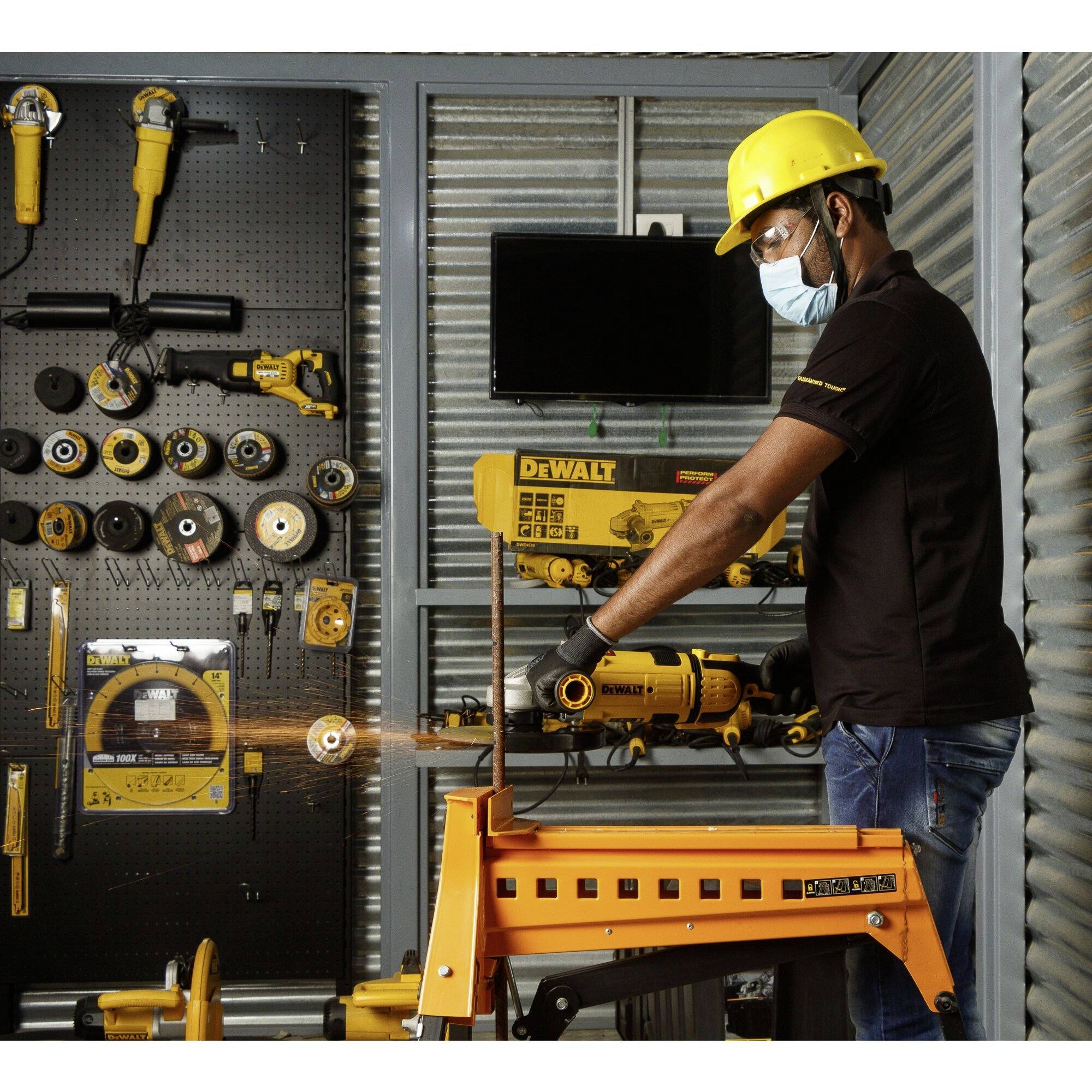 A man wearing a safety helmet and mask working with a grinding machine, surrounded by various tools in a workshop.