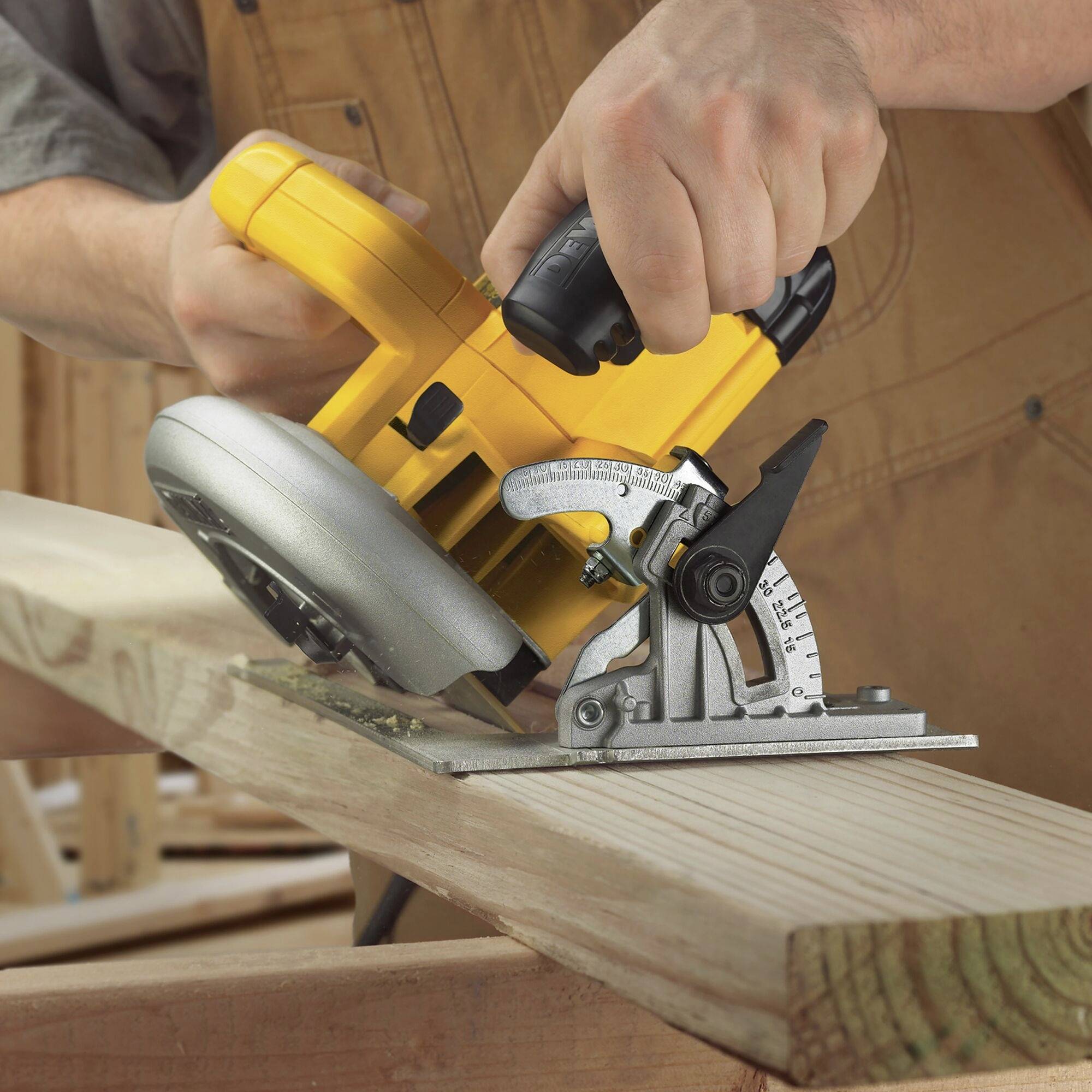 A person is sawing a plank with a yellow circular hand saw in a woodworking workshop.