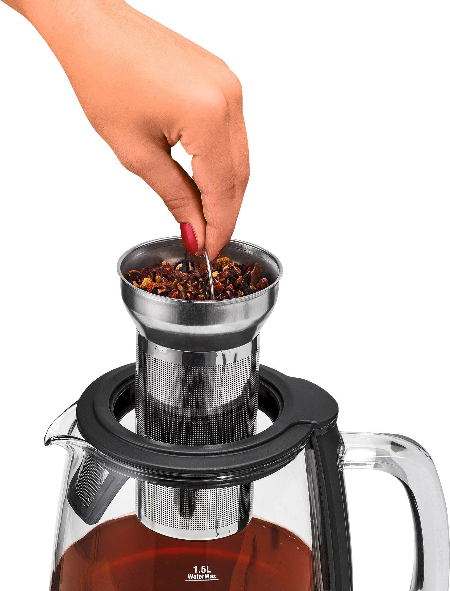 A hand is holding a tea strainer over a glass jug filled with brewed tea.
