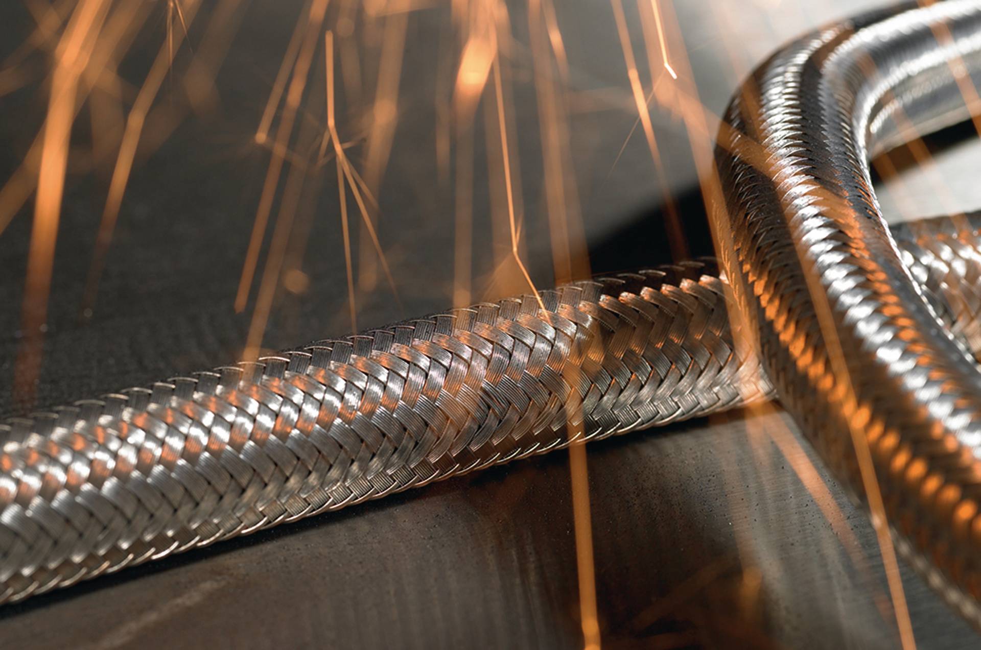 Braided metal hose with sparks in the background, demonstrating an industrial application.