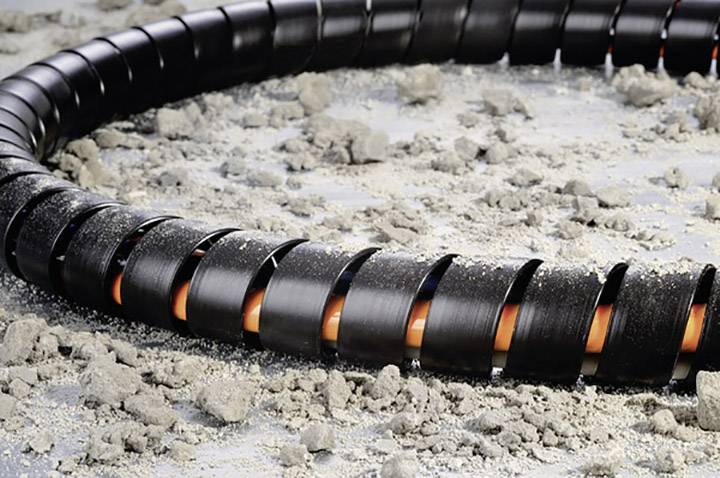 A spiral-shaped protective sleeve lies on a sandy surface, partially concealing an orange cable within it.