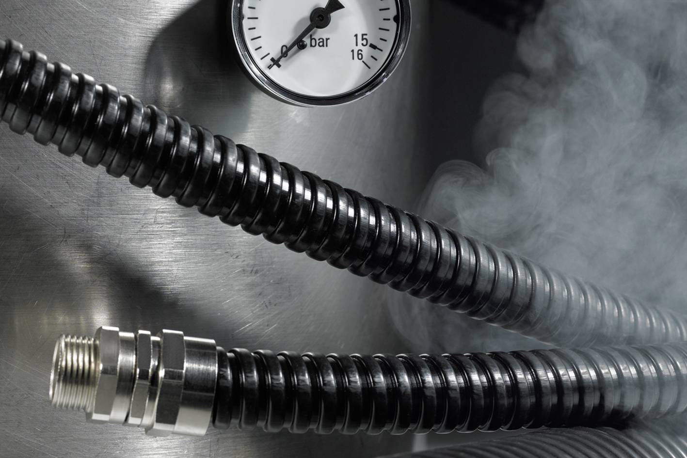 Steam hose with measuring device, showing 2 bar pressure, surrounded by steam in a metallic environment.