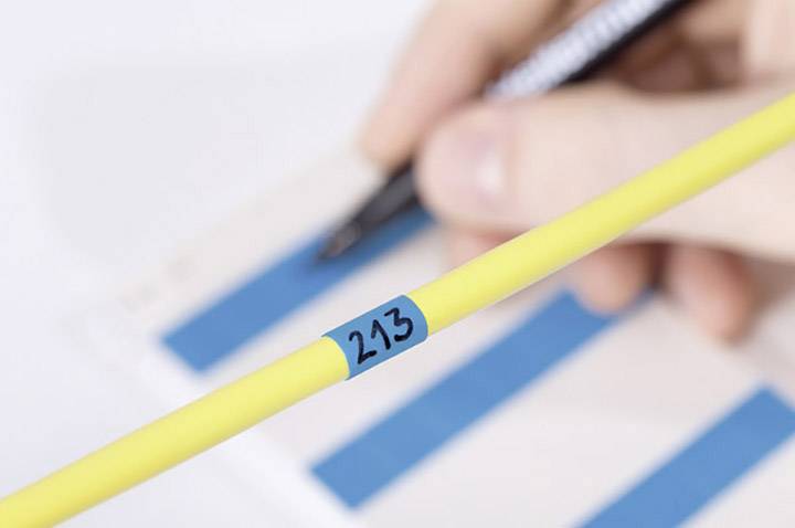 Yellow cable with the number '243' in the foreground; in the background, a hand holds a pen over a checklist.
