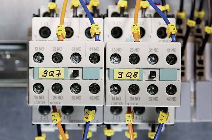 An electrical cabinet with two identifiable switching relays, labelled as '9Q7' and '9Q8', with connected coloured cables.