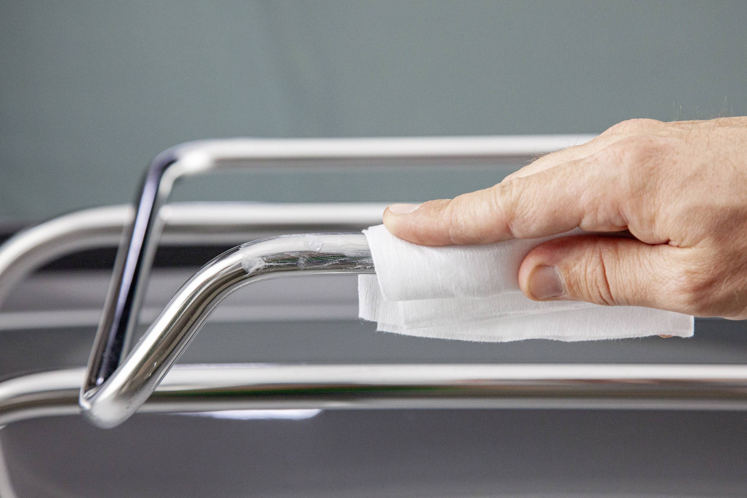 A hand is cleaning a metal bar with a white cloth.