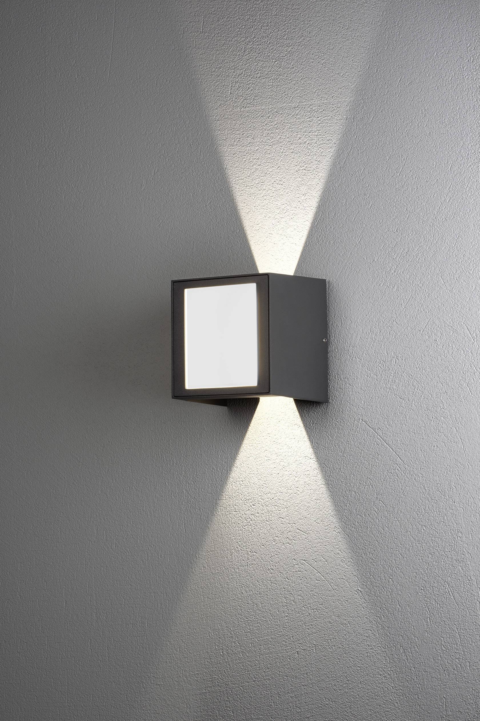 Modern black wall light on a grey wall, casting light upwards and downwards. Suitable for stylish interior lighting.